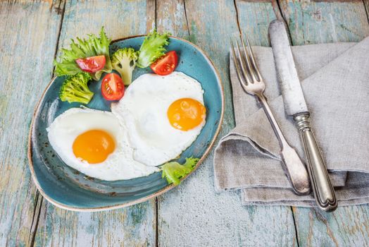 Breakfast in rustic style, consists of fried eggs and raw vegetables on the old wooden table