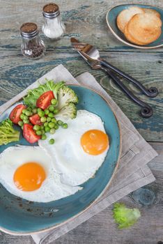 Breakfast consists of fried eggs, fresh vegetables and toasts on the old wooden table