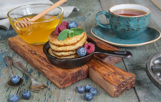 Breakfast in rustic style: pancakes in cast-iron frying pans,  honey, fresh berries and black tea 