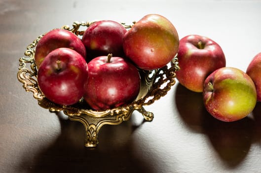 A metal vase full of red apples casts a contrasting shadow