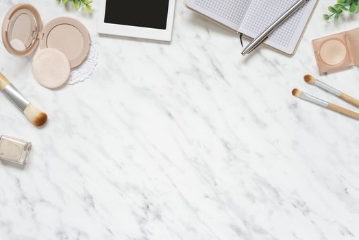 Feminine workspace on table desk with smartphone, notebook, pen, compact powder, cosmetic brushes and nail polish on marble stone background; top view, flat lay