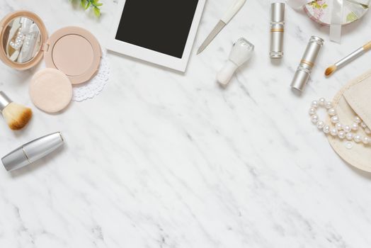 Feminine workspace on table desk with smartphone, lipstick; pearl necklace, compact powder, cosmetic brushes and nail polish on marble stone background; top view, flat lay