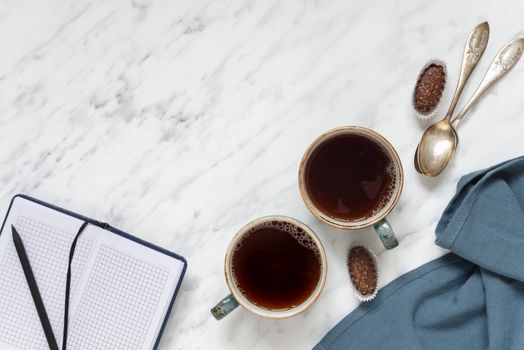 Morning composition with two cups of black coffee, blue napkin and notebook on a marble surface, with space for text, top view