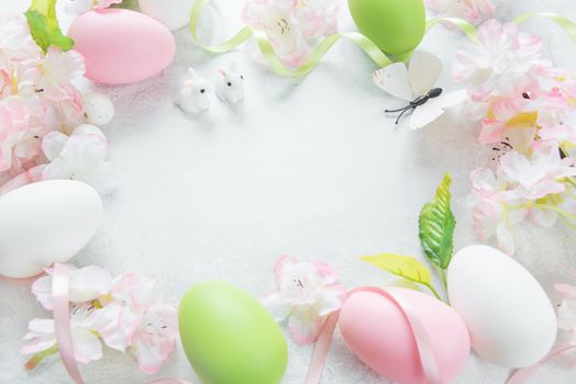 Beautiful delicate Easter frame with pink cherry flowers, multicolored Easter eggs, Easter bunny and butterfly on the stone background, with copy-space