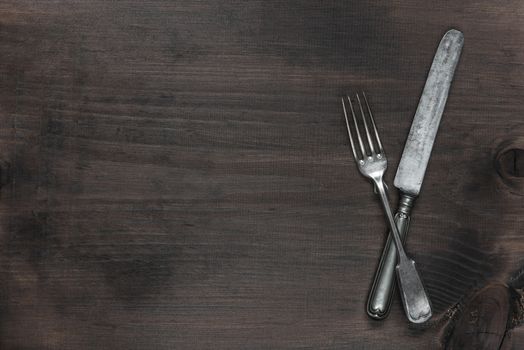 Crossed vintage silver fork and knife on the background of old brown wooden board, with copy-space