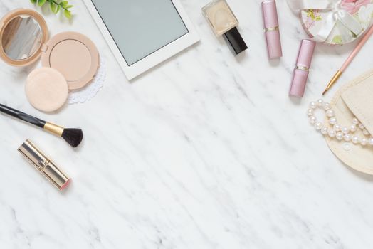 Feminine workspace on table desk with smartphone, lipstick; pearl necklace, compact powder, cosmetic brushes and nail polish on marble stone background; top view, flat lay