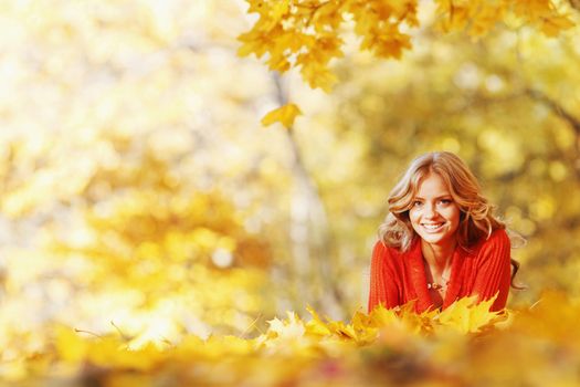 Happy young woman laying on autumn leaves in park