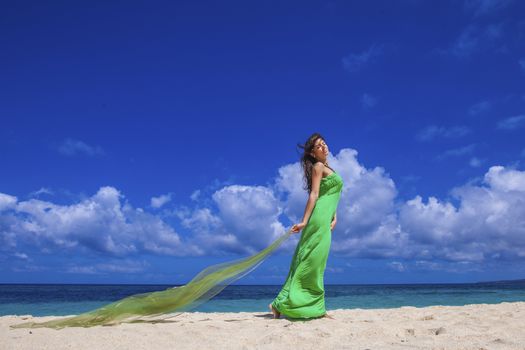 Woman in green dress posing with fabric in tropical sea beach