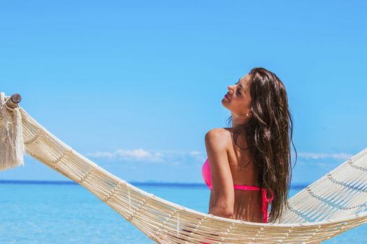 Young woman swinging in hummock on blue sea background
