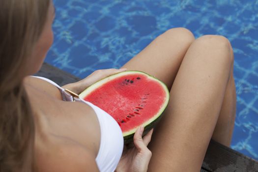 Girl holding watermelon in the blue pool, slim legs. Tropical fruit diet. Summer holiday idyllic.