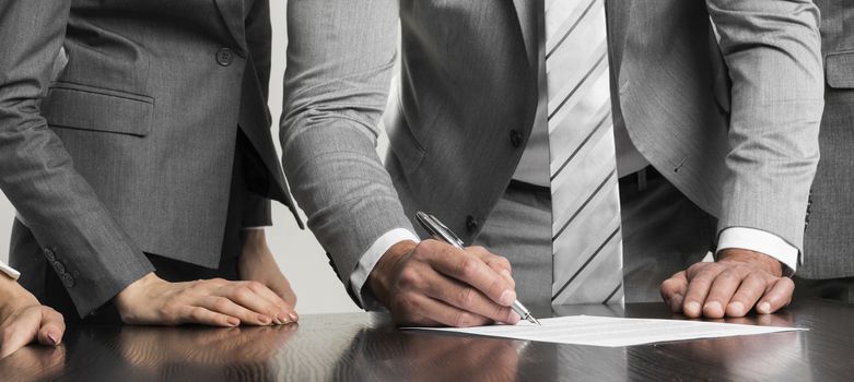 Businessman signing contract while his team is looking at him