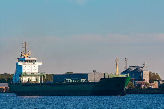 Green cargo ship leaves the port in a clear day