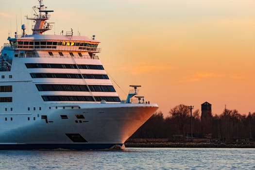 White passenger ship moving against the orange sunset sky