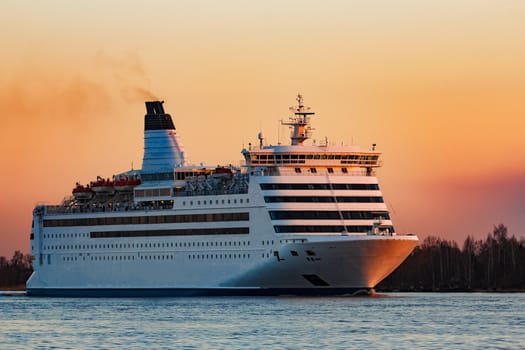 White passenger ship moving against the orange sunset sky