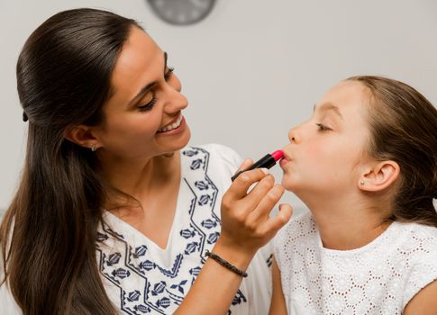 Mother playing with her daughter applying lipstick