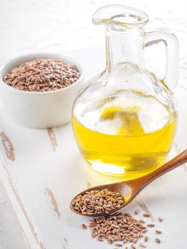 Brown flax seeds in spoon and flaxseed oil in glass bottle on white wooden background. Flax oil is rich in omega-3 fatty acid.