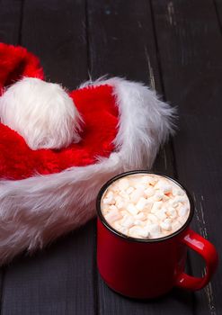 Hot chocolate with marshmallows and cap santa on grunge dark table