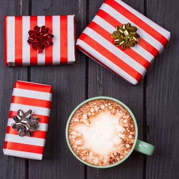 cup of hot cocoa or chocolate with marshmallow and gift boxes on wooden table from above