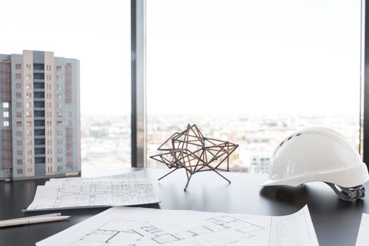 Building model, blueprint and hardhat at office table