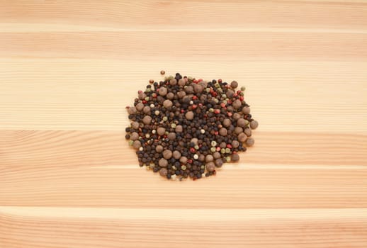 Mixed peppercorns - black, white, pink, green, pimento - on a wooden background, pine wood grain
