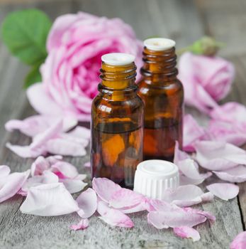 Two vials with essential oil and petals of pink roses on a wooden background