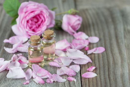 Two vials with essential oil and petals of pink roses on a wooden background