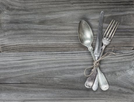 Crossed vintage fork, table knife and spoon on old wooden boards