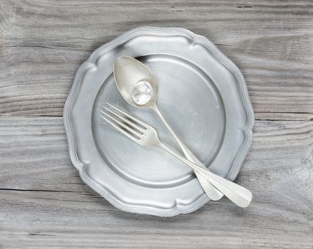 Big diamond, vintage fork and spoon in an empty tin plate on an old wooden table