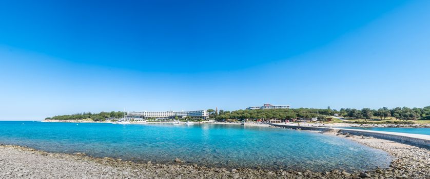 Seaside hotel with beach and turquoise water, Sveti Andrija or Red island near Rovinj, Croatia. A dike connects the island with Miskin island.