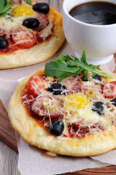 Mini pizza with sausage and egg and arugula, a cup of coffee 