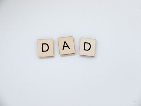 The word "Dad" spelled out with wooden letter tiles.