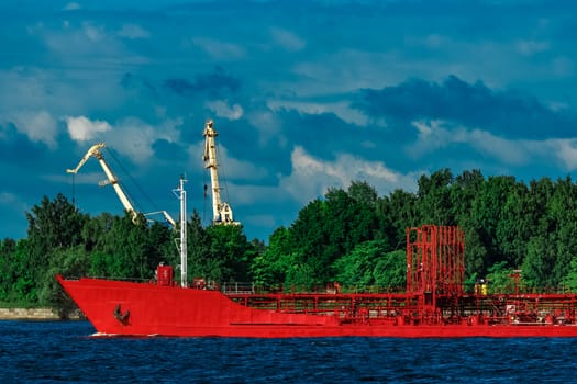 Red cargo tanker ship moving by the river