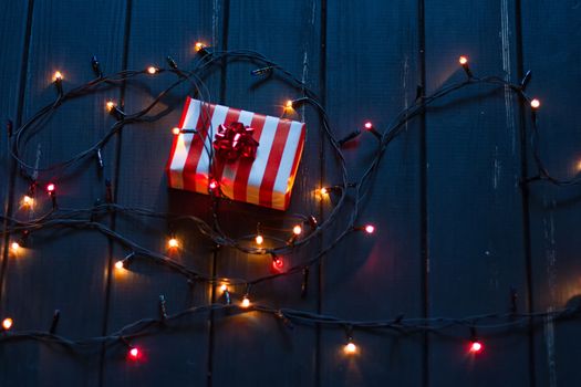 Gift box and garland lights over old wooden background