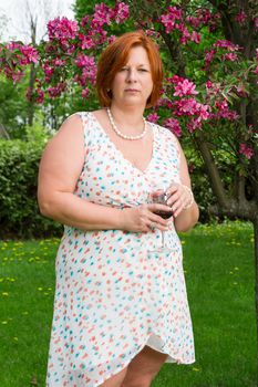 forty year old woman in summer dress, having a glass of wine under a cherry tree