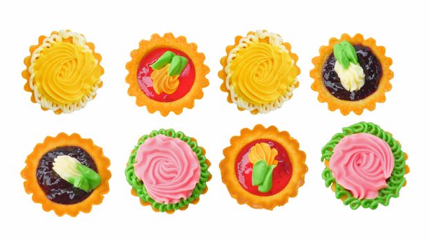 Two Rows of Delicious Little Tarts with Colored Butter Cream, Fruit Jam and Decoration isolated on White background. Top View
