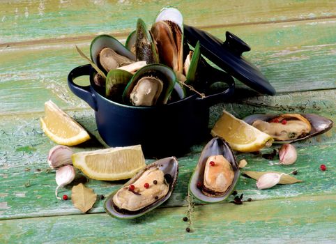 Arrangement of Fresh Boiled Green Mussels with Spices and Lemon in Dark Pannikin closeup on Green Wooden background