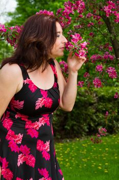 forty something brunette woman wearing a sun dress smelling flower from a cherry tree