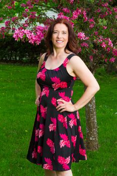forty something brunette woman wearing a sun dress standing under a cherry tree