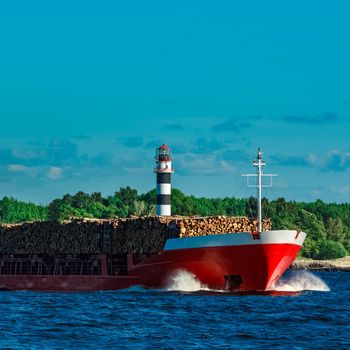 Red cargo ship fully loaded with wood moving at clear day