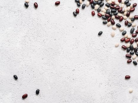 Top view of raw mixed beans on gray concrete background. Mixed of uncoocked black, red and white beans with copy space. Fodd background. Vegan protein concept.