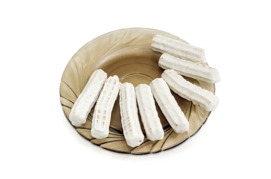 Several shortbread cookies in the form of sticks glazed with white chocolate on a glass saucer on a light background
