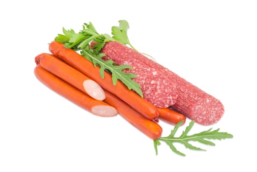 Several long thin smoked hunting frankfurters and partly sliced salami with several arugula and parsley leaves on a light background
