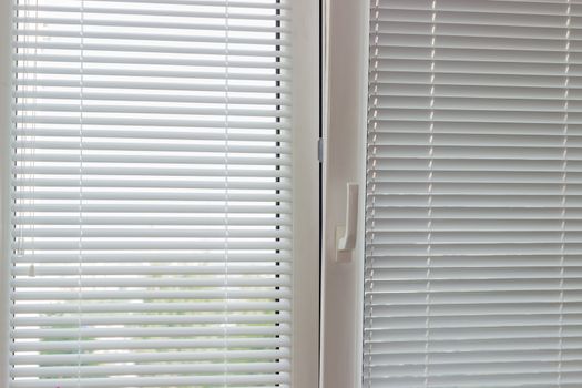 Fragment of thr modern tilt and turn plastic window with white Venetian blinds with manual control
