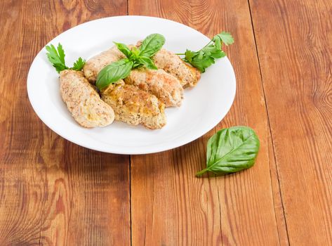 Eastern European dish zrazy - braised meat roulades with filling from bread dried crusts and mushrooms decorated with basil and parsley twigs on a white dish on a surface of an old wooden planks
