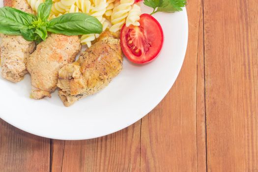 Top view of part of the white dish with stuffed braised meat roulades, spiral pasta and tomato decorated with herbs on a surface of an old wooden planks
