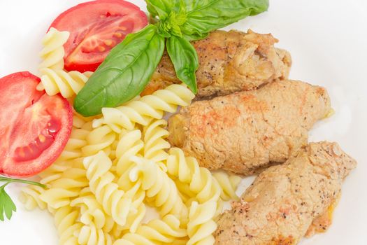 Top view of the braised stuffed meat roulades, spiral pasta and tomato, decorated with basil and parsley twigs closeup
