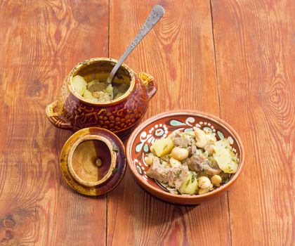 Ukrainian version of the dish Chanakhi in a clay bowl  - potatoes with meat, mushrooms and haricot beans roasted in a clay pot on a surface of an old wooden planks
