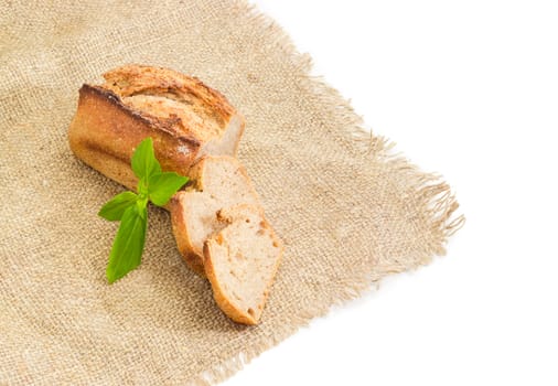 Partially cut wheat sourdough bread with basil twig on a sackcloth on a white background
