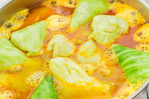 Background of the stuffed cabbage rolls in boiling sauce in large stainless steel saucepan during cooking
