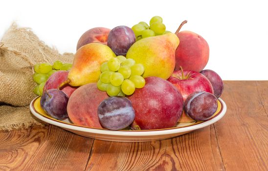 Pile of the apples, pears, plums, peaches and clusters of white grapes on the big yellow dish on a surface of old wooden planks with sackcloth on a white background
